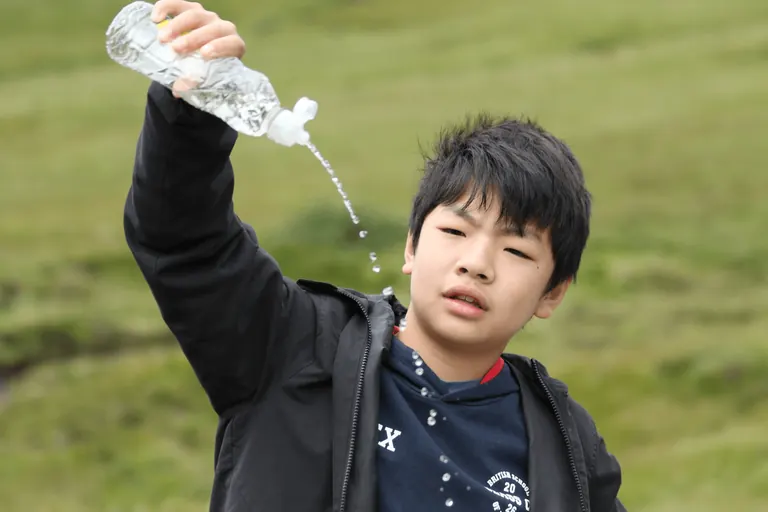 孩子举起装有 Fairy Pools 溪水的透明水瓶