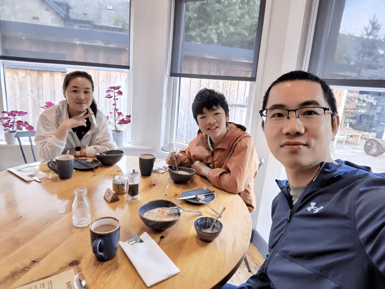 一家三口在 Ravenscraig Guest House 圆桌前自拍,桌上是麦片碗、咖啡杯与桌号 7。