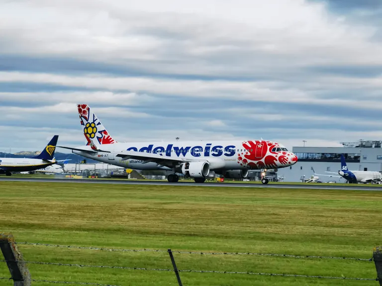 Edelweiss Air 客机 HB-JLT 在跑道上,机头红色手印涂装,前景铁丝网。