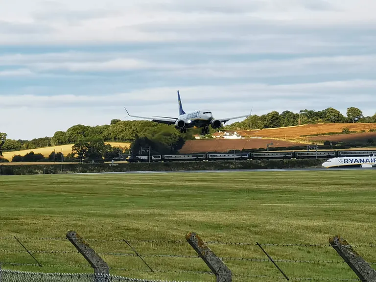 Ryanair 客机五边进场,起落架放下,背景是列车与丘陵农田。