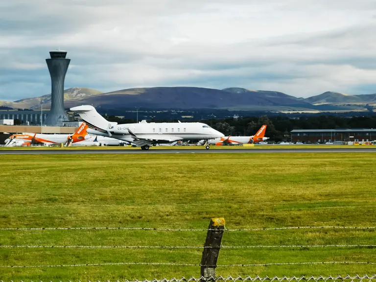 白色公务机 CS-CHK 在跑道上,后方可见 easyJet 与爱丁堡塔台。
