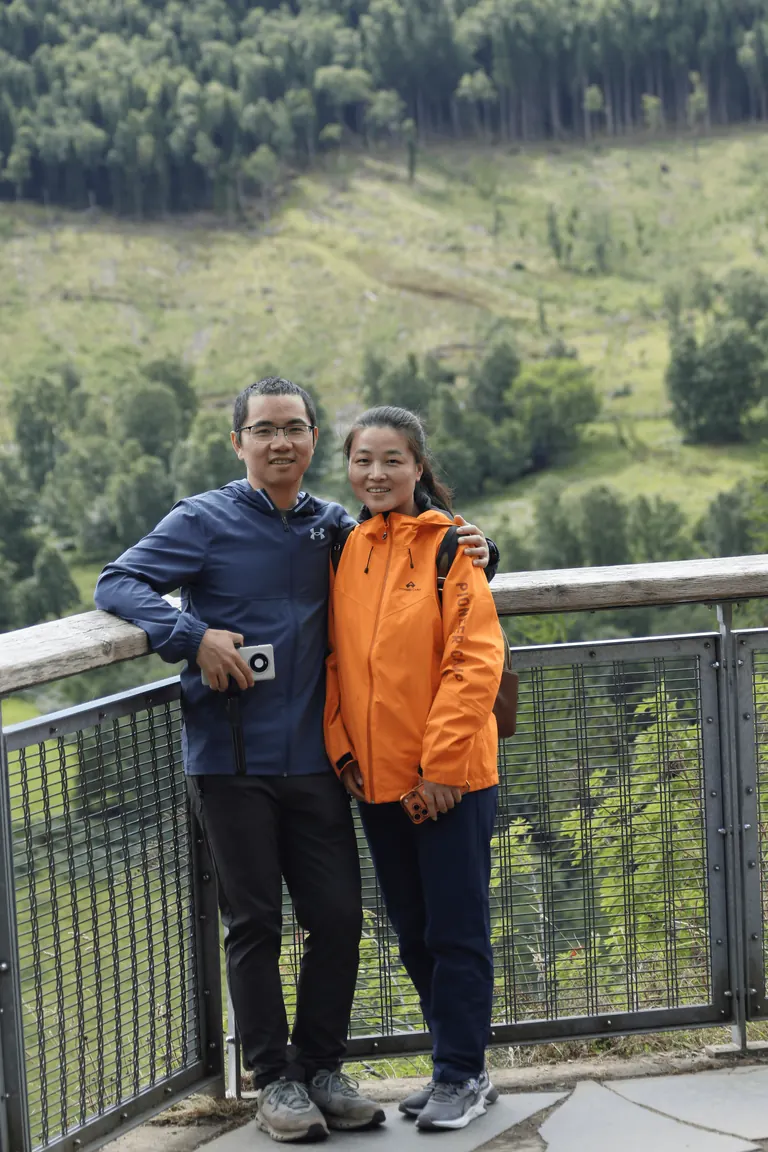 Martin 与 Spring 站在 Queen's View 木质栏杆后合影,身后是林坡。