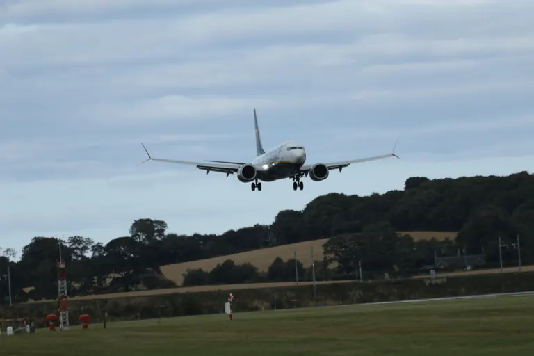 Ryanair 客机正对镜头五边进场,起落架与着陆灯打开,背景是丘陵农田。