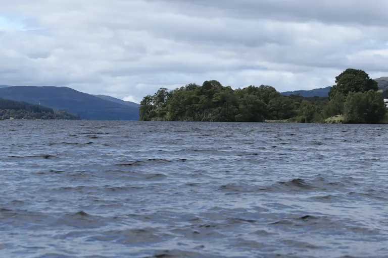 从 Loch Tummel 水边看对岸密林半岛与远山,近处湖面起细浪。
