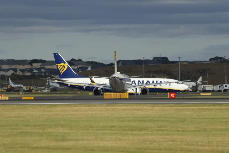 两架 Ryanair 客机与 A15 滑行道牌,远处是坡上住宅。