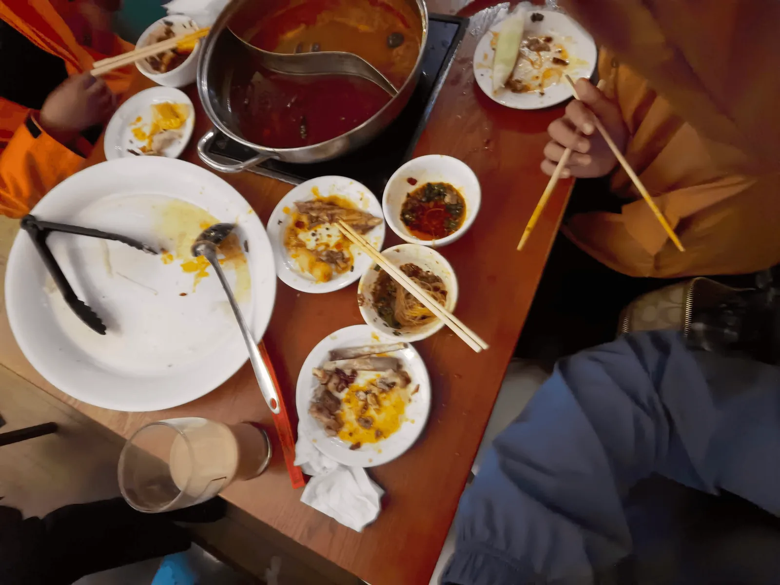 用餐将尽时的鸳鸯锅锅底、餐盘与一家人的手