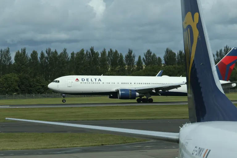 Delta 涂装客机位于跑道区域,前景是另一架客机的垂直尾翼。